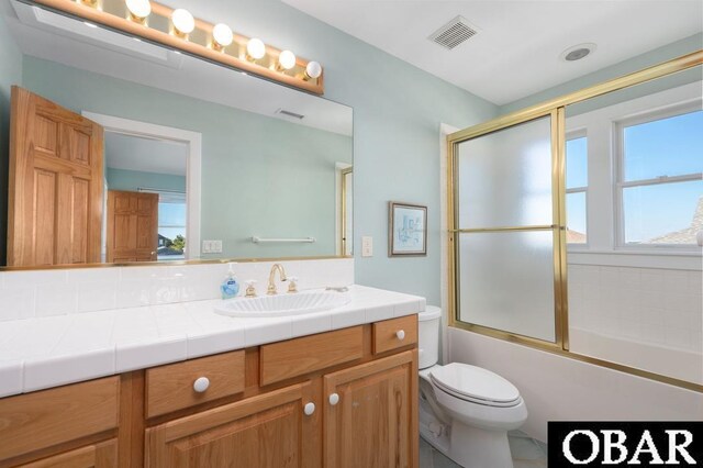 full bathroom with visible vents, bath / shower combo with glass door, toilet, and vanity