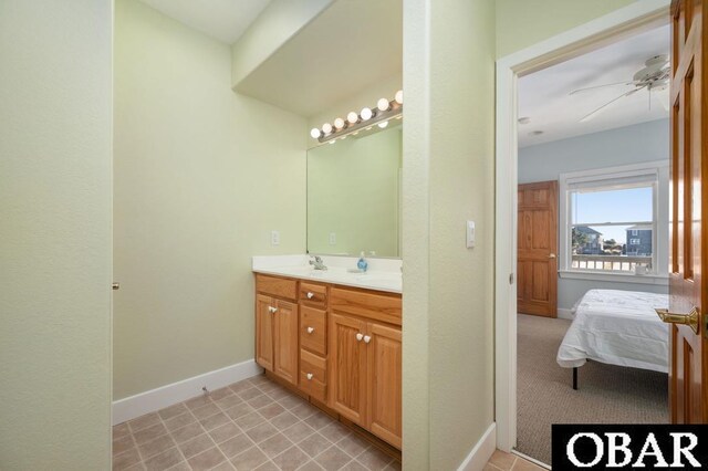 ensuite bathroom featuring baseboards, double vanity, ceiling fan, a sink, and ensuite bathroom