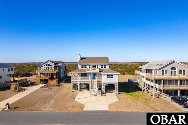 view of front of house with driveway, a balcony, stairway, a carport, and a chimney