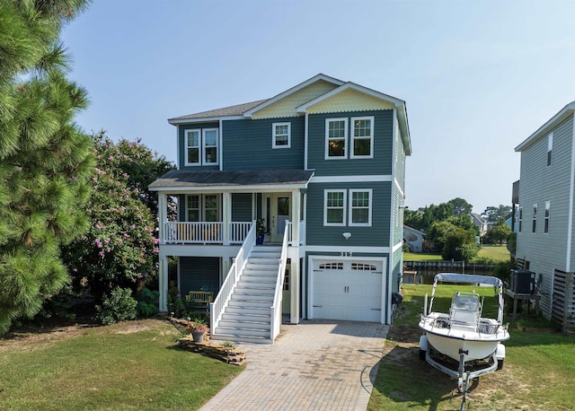 beach home with a porch, an attached garage, stairs, decorative driveway, and a front yard