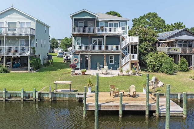 rear view of property with a patio, a fire pit, a deck with water view, stairs, and a lawn