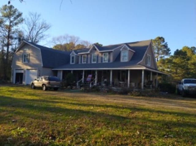 view of front of house featuring a garage, covered porch, a front lawn, and a gambrel roof