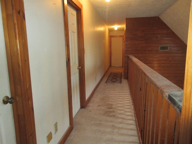 hallway with visible vents, vaulted ceiling, and a textured ceiling