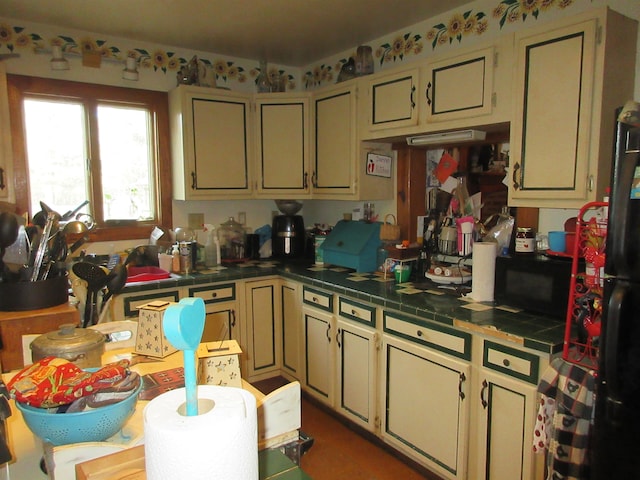 kitchen with tile countertops, cream cabinets, black microwave, and freestanding refrigerator