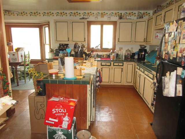 kitchen with cream cabinetry, dark countertops, freestanding refrigerator, and a healthy amount of sunlight