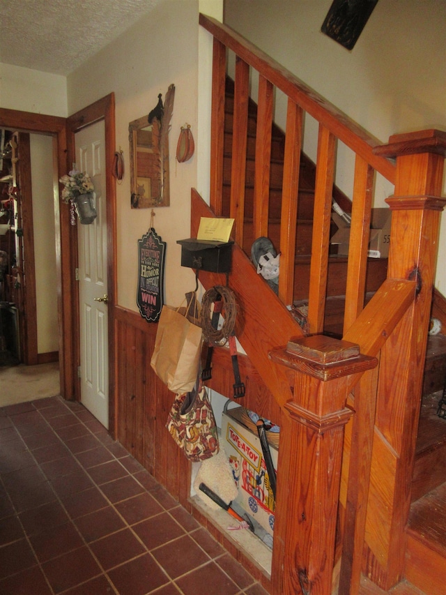 corridor with a textured ceiling, wood walls, stairway, and wainscoting