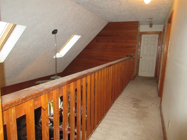 hallway with vaulted ceiling, a textured ceiling, light colored carpet, and wooden walls