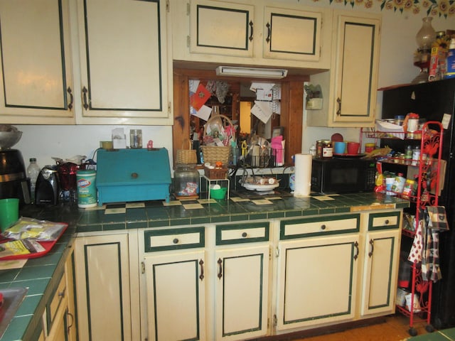 kitchen featuring tile countertops, cream cabinetry, and black microwave