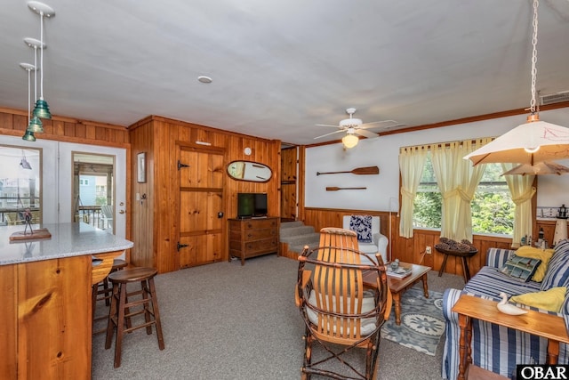 living room with ceiling fan, crown molding, a wainscoted wall, wood walls, and light colored carpet
