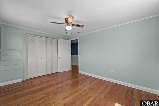unfurnished bedroom with wood finished floors, visible vents, a closet, crown molding, and baseboards