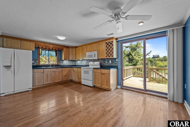 kitchen with dark countertops, a sink, white appliances, light wood-style flooring, and a textured ceiling