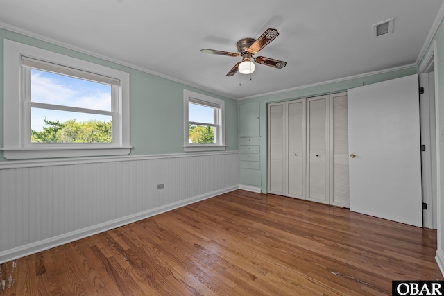 unfurnished bedroom with crown molding, wood finished floors, a closet, ceiling fan, and visible vents