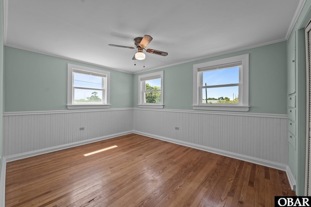 empty room featuring wainscoting, hardwood / wood-style flooring, ceiling fan, and crown molding