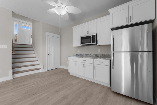 kitchen with light wood-type flooring, white cabinetry, appliances with stainless steel finishes, baseboards, and light stone countertops