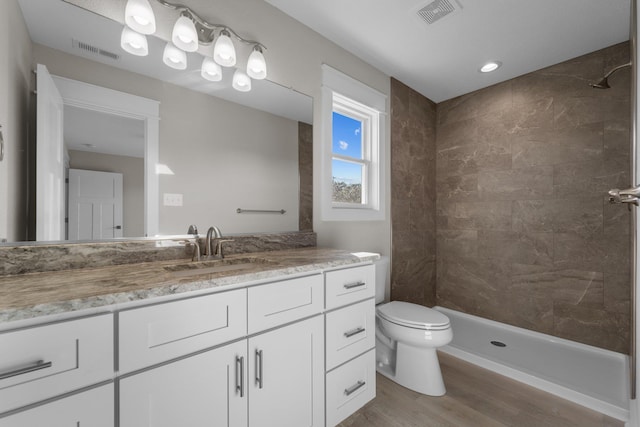 full bathroom featuring visible vents, tiled shower, wood finished floors, and vanity