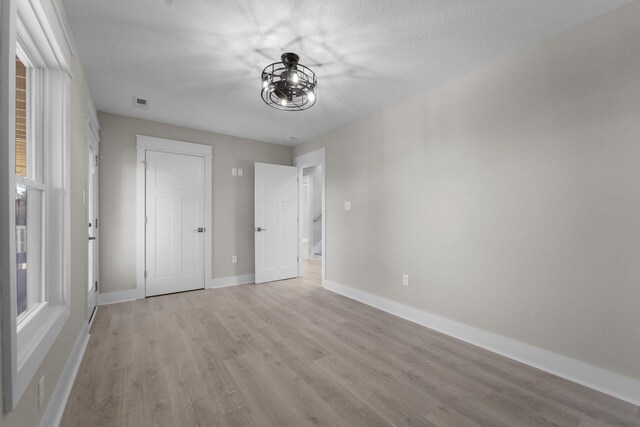 unfurnished bedroom with visible vents, light wood-style flooring, an inviting chandelier, and baseboards