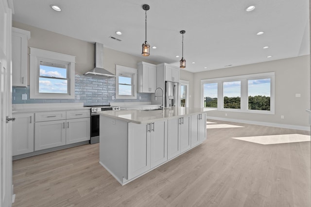 kitchen with a sink, light countertops, appliances with stainless steel finishes, wall chimney exhaust hood, and a kitchen island with sink