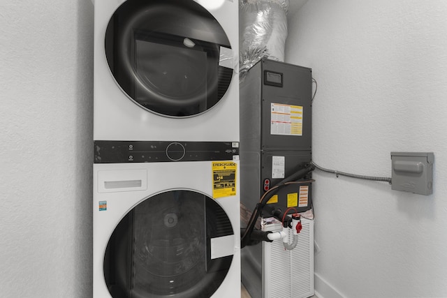 clothes washing area with a textured wall, laundry area, and stacked washer / dryer