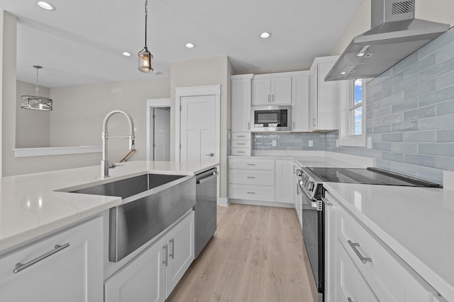 kitchen with a sink, stainless steel appliances, pendant lighting, white cabinetry, and wall chimney range hood