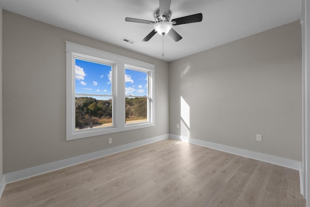 empty room with light wood finished floors, visible vents, a ceiling fan, and baseboards