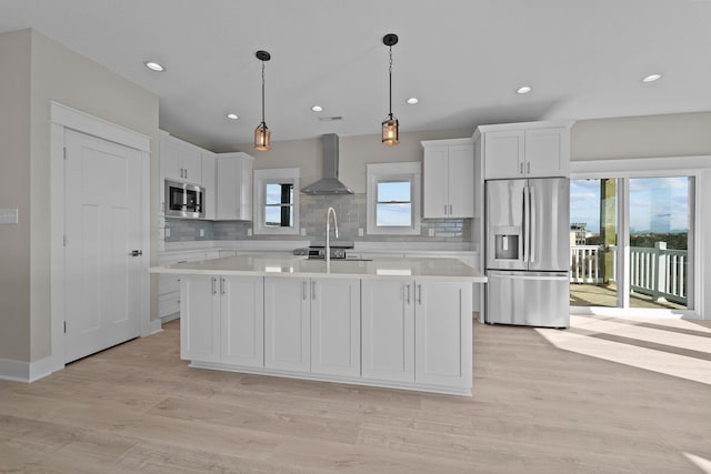 kitchen with light wood-type flooring, wall chimney range hood, stainless steel appliances, white cabinets, and light countertops