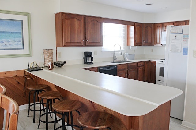 kitchen with light countertops, a sink, white appliances, a peninsula, and a kitchen breakfast bar