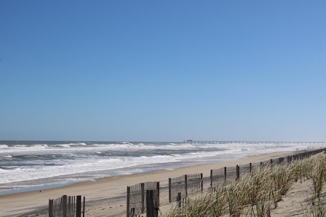 water view featuring fence and a beach view