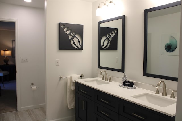 full bathroom featuring double vanity, wood finished floors, a sink, and baseboards