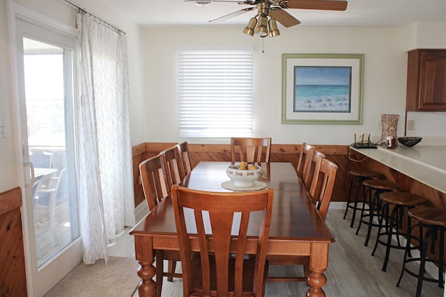 dining room with a wainscoted wall, ceiling fan, wooden walls, and wood finished floors