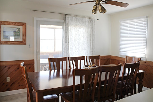 dining room with ceiling fan, wooden walls, and wainscoting