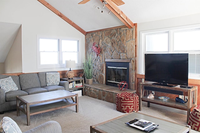 carpeted living area with a ceiling fan, a stone fireplace, and lofted ceiling with beams