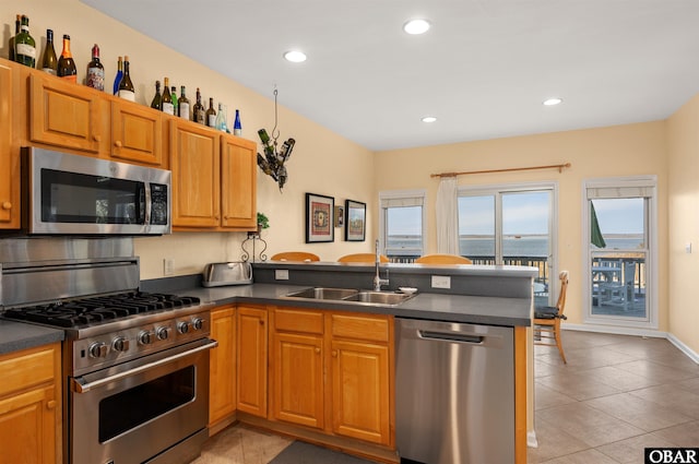 kitchen with a peninsula, appliances with stainless steel finishes, dark countertops, and a sink