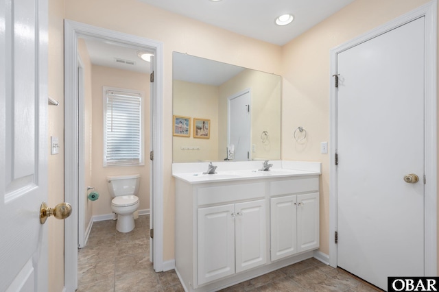 full bath with toilet, double vanity, baseboards, and a sink