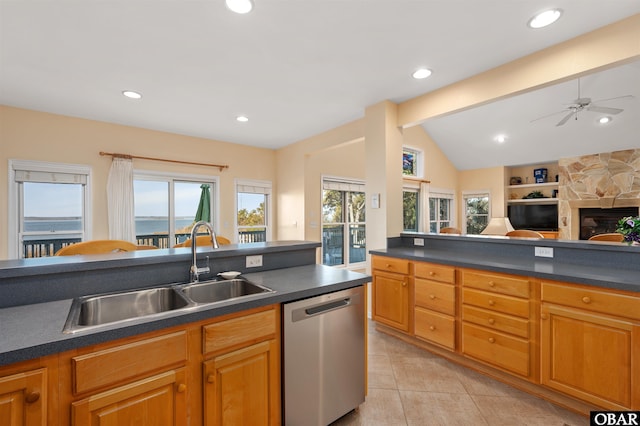 kitchen featuring dark countertops, stainless steel dishwasher, open floor plan, a sink, and a stone fireplace