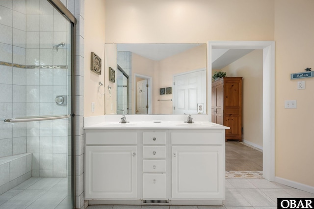 full bathroom featuring double vanity, baseboards, a sink, and tiled shower