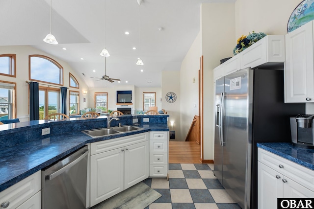 kitchen with white cabinets, dark countertops, stainless steel appliances, light floors, and a sink