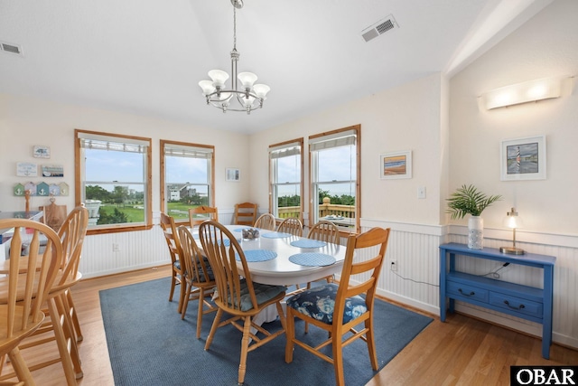 dining area with light wood-style floors, wainscoting, visible vents, and an inviting chandelier