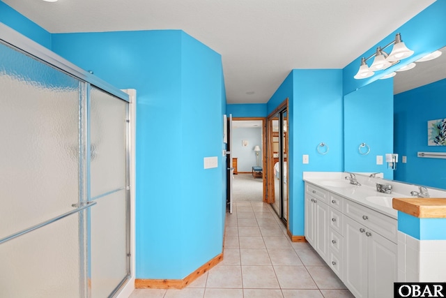 ensuite bathroom with double vanity, a sink, a shower stall, ensuite bath, and tile patterned flooring