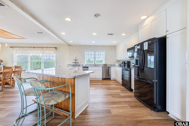 kitchen featuring light wood finished floors, visible vents, a breakfast bar area, black appliances, and white cabinetry