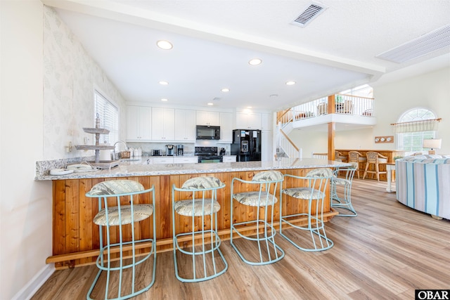 kitchen featuring black appliances, a peninsula, a sink, and light wood-style floors