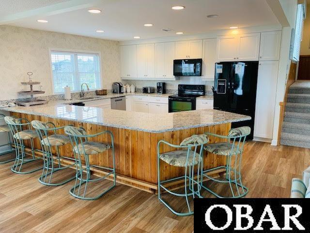 kitchen with light stone countertops, black appliances, white cabinets, and a kitchen breakfast bar