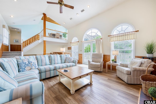 living room with a wainscoted wall, light wood finished floors, visible vents, stairway, and wood walls