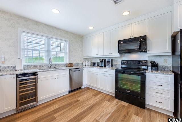 kitchen with a sink, light wood-type flooring, beverage cooler, black appliances, and wallpapered walls