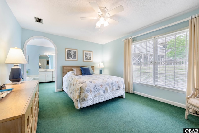 carpeted bedroom featuring arched walkways, a textured ceiling, ensuite bathroom, visible vents, and baseboards