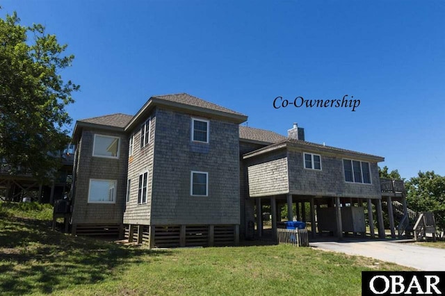 view of front of property featuring a chimney, a shingled roof, concrete driveway, a carport, and a front lawn