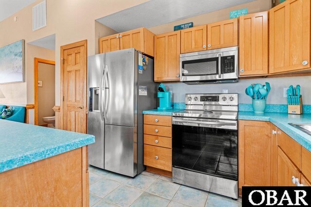 kitchen with light countertops, appliances with stainless steel finishes, light brown cabinets, and visible vents