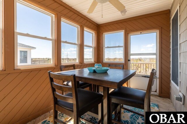 dining area featuring wood walls, ceiling fan, and wood finished floors