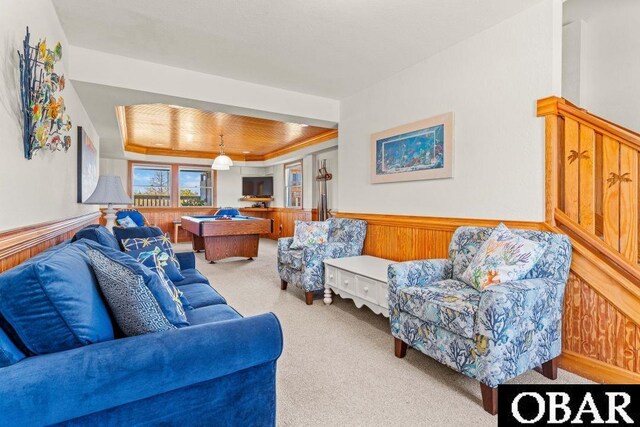 living room featuring a raised ceiling, wainscoting, wood walls, and light carpet