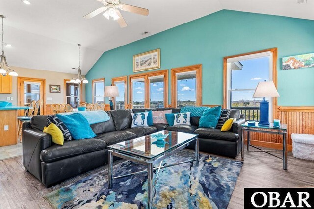 living room featuring vaulted ceiling, a wainscoted wall, ceiling fan with notable chandelier, and wood finished floors