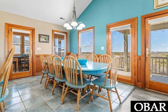 dining space featuring a chandelier, lofted ceiling, wainscoting, and visible vents